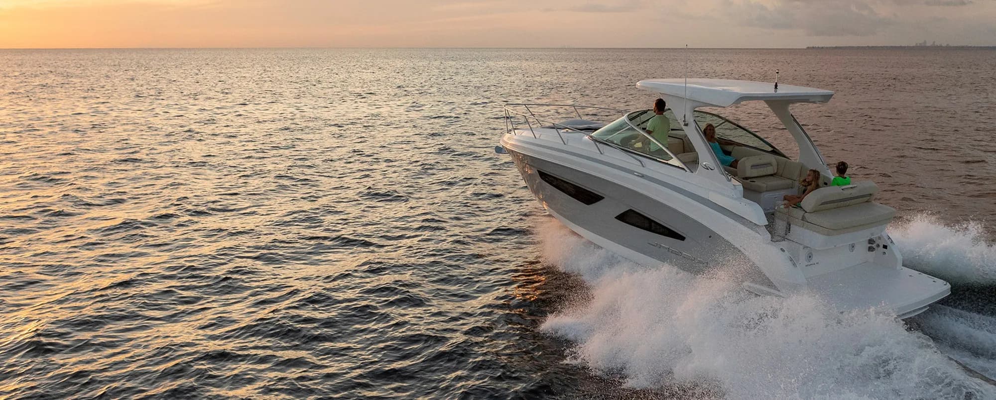 An express cruiser with a family aboard throwing spray across open water at sunset