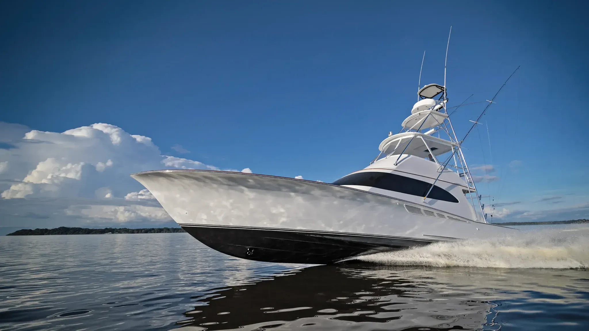 A white sportfishing boat with a tuna tower and outriggers running fast across calm water under a blue sky